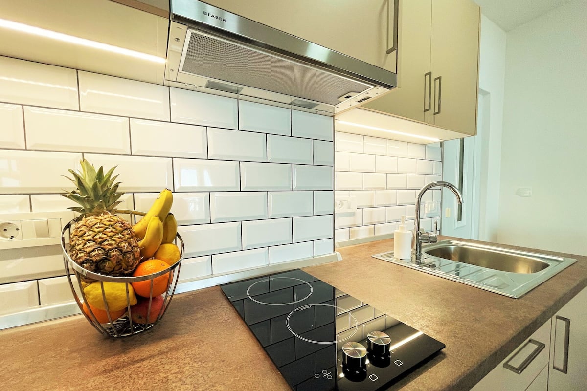 A modern kitchen with white subway tiles, a stainless steel range hood, a built-in gas stove, and a fruit bowl on the counter.