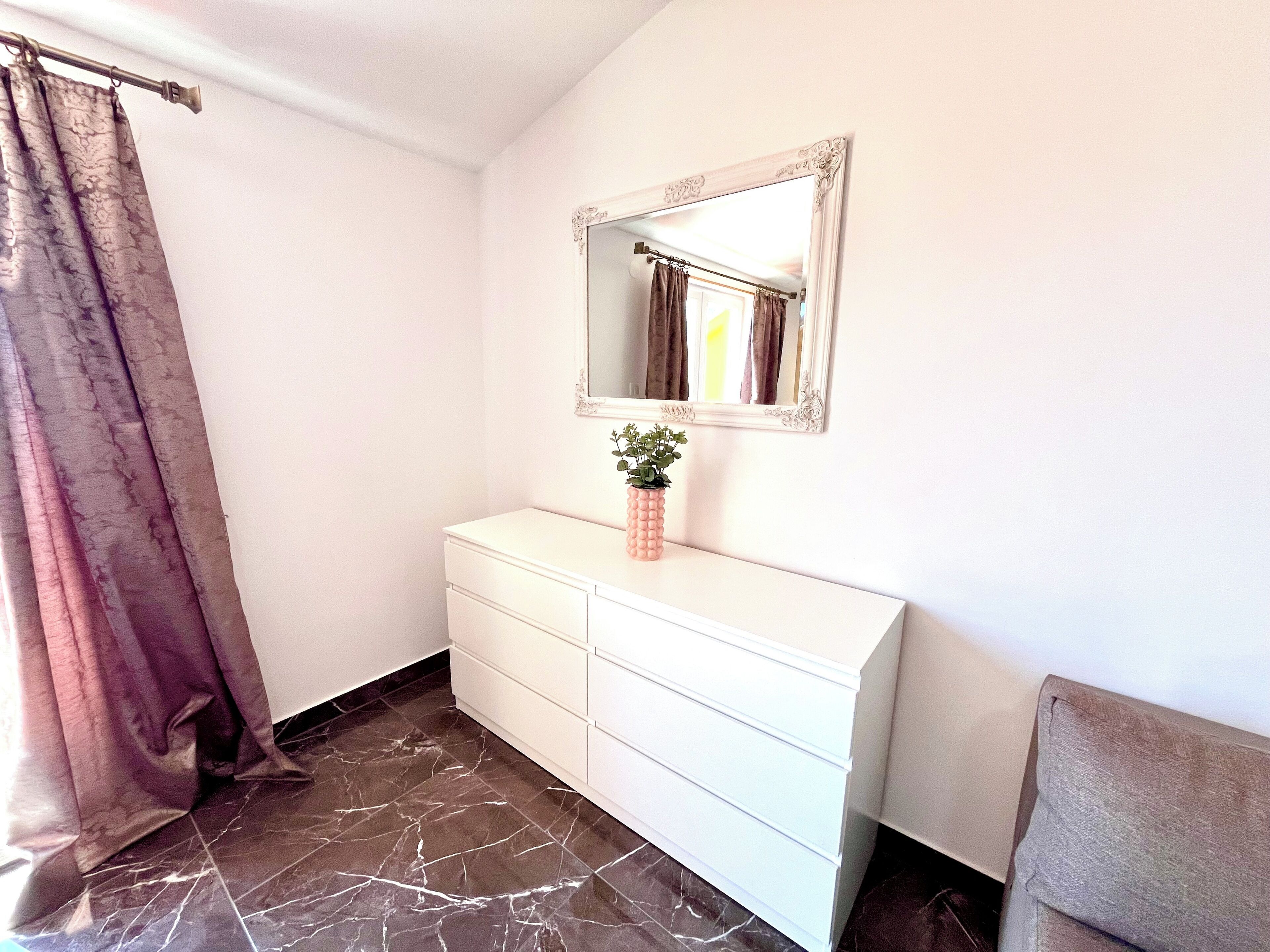 A bathroom with a white vanity, a mirror with an ornate frame, a potted plant, and a shower curtain.