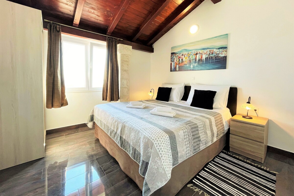 A hotel room with a bed, bedside table, lamp, and a painting on the wall.