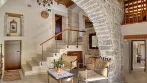 A stone-walled interior with a staircase, a wooden door, a table with a plant, and a cushioned chair. - Amari Villas: calm and comfort in the real Crete (Rethymno)