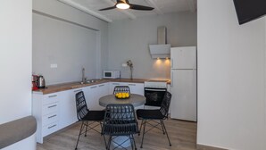 Cozinha compacta com armários brancos, micro-ondas, fogão e ventilador de teto. Há uma mesa de jantar com cadeiras e uma tigela de frutas.