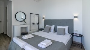 Quarto de hotel moderno com uma cama grande, uma mesinha de cabeceira, um espelho e uma pequena mesa redonda.