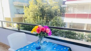 Un balcón con una mesa cubierta por un mantel azul, una silla blanca y un jarrón con flores de colores.