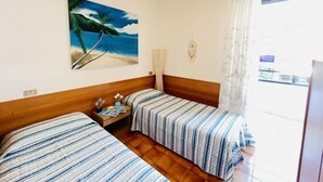 Habitación de hotel con dos camas, un cuadro de una playa, una ventana con cortinas y un cabecero de madera.