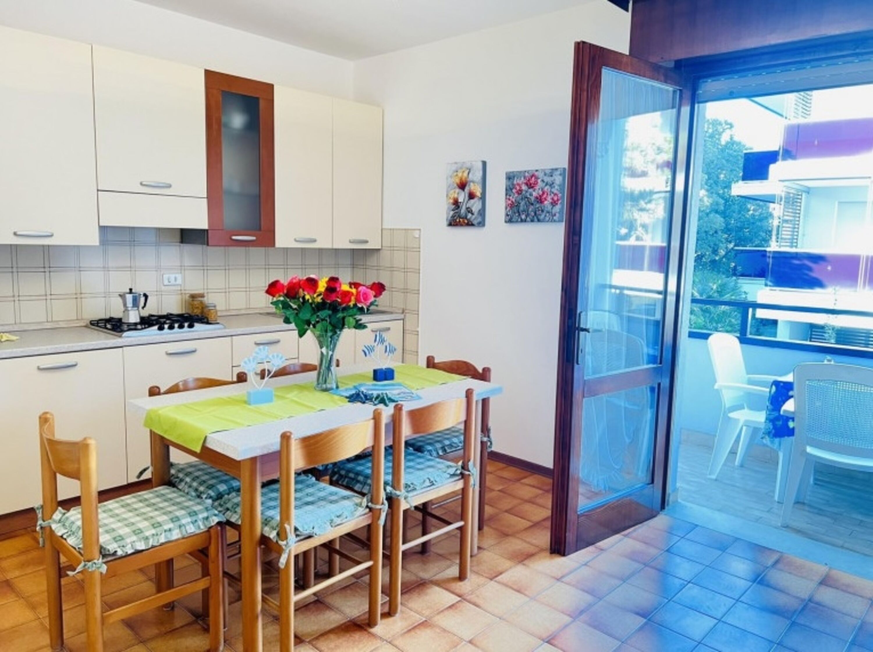 A kitchen with white cabinets, a dining table with chairs, a vase of flowers, and a sliding glass door leading to an outdoor area.
