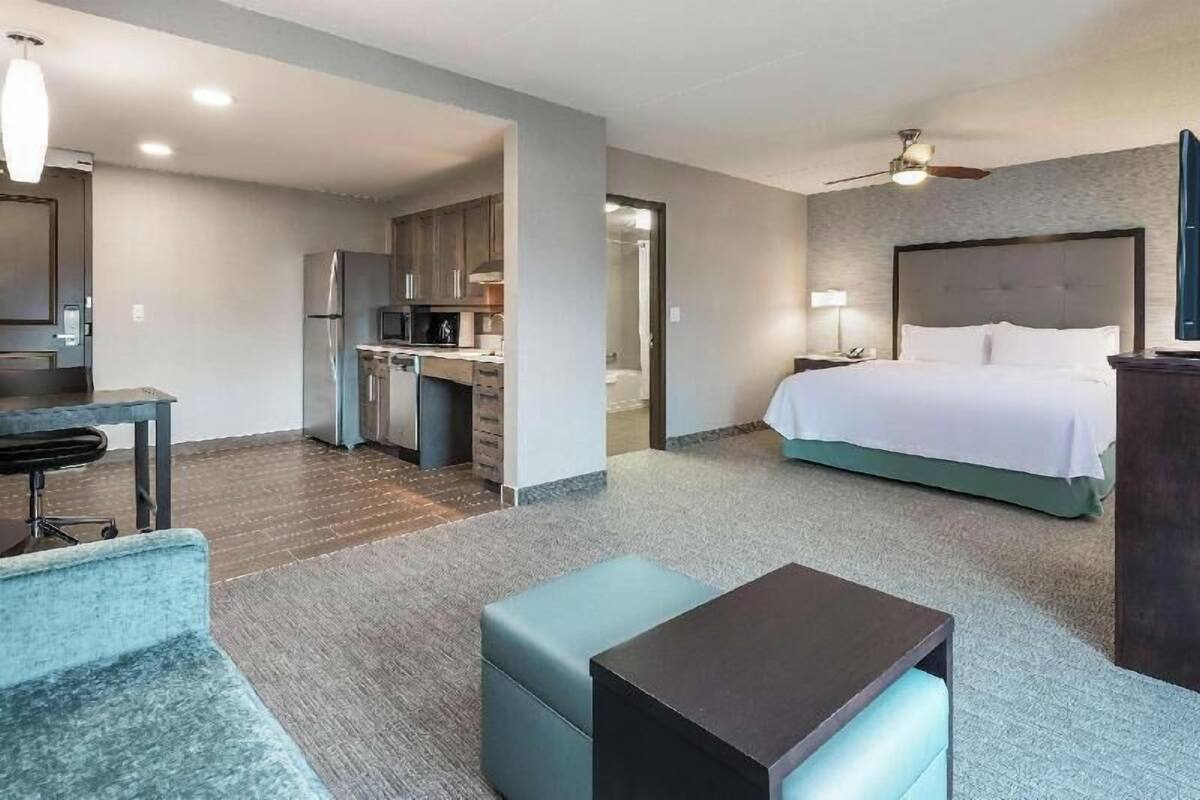 Habitación de hotel con cama, escritorio, kitchenette y zona de estar separada.