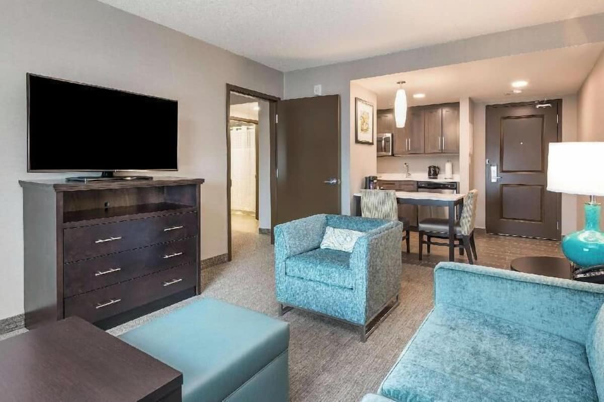 A hotel room with a TV, a sofa, a chair, a small table, and a kitchenette.