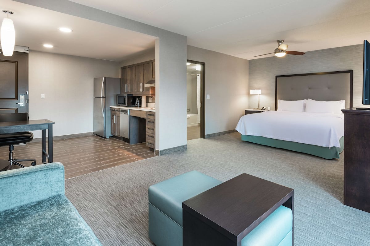 A hotel room with a bed, a desk, a kitchenette, and a seating area.