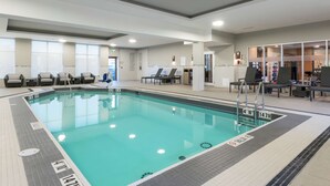 Una piscina interior con carriles delimitados, sillas de descanso y suelo de baldosas.