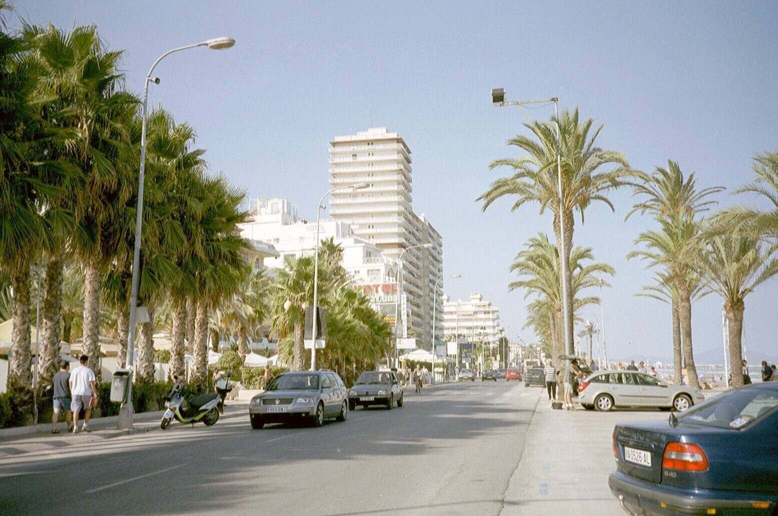 Una calle costera bordeada de palmeras y edificios, incluyendo un hotel con varios pisos y balcones.