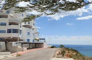 Un edificio frente al mar con varios balcones, una zona de estacionamiento techada y vistas al océano.