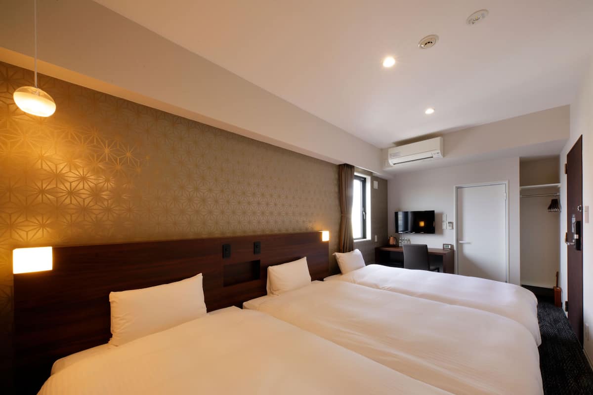 Ein Hotelzimmer mit einem großen Bett, einem Schreibtisch mit Stuhl, einem Fernseher und einer Klimaanlage.