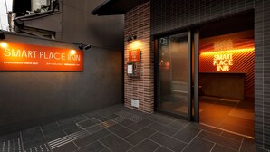 The exterior of a hotel with a sign reading "SMART PLACE INN" and a modern design with a brick facade and glass entrance. - Smart Place Inn Kyoto Shijo Omiya East (Kyoto)