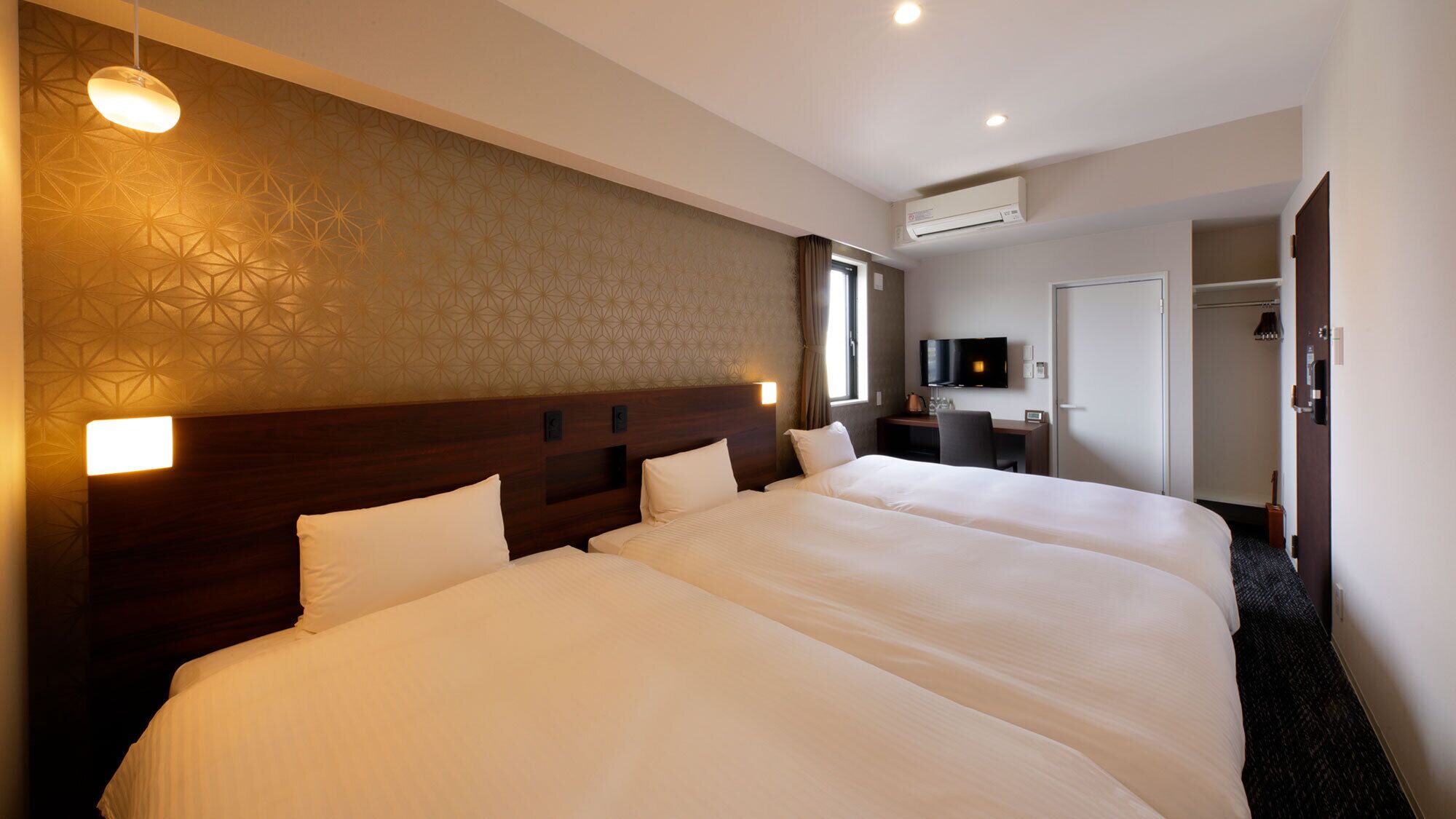 Ein Hotelzimmer mit zwei großen Betten, einem Schreibtisch mit Fernseher und einer Klimaanlage.