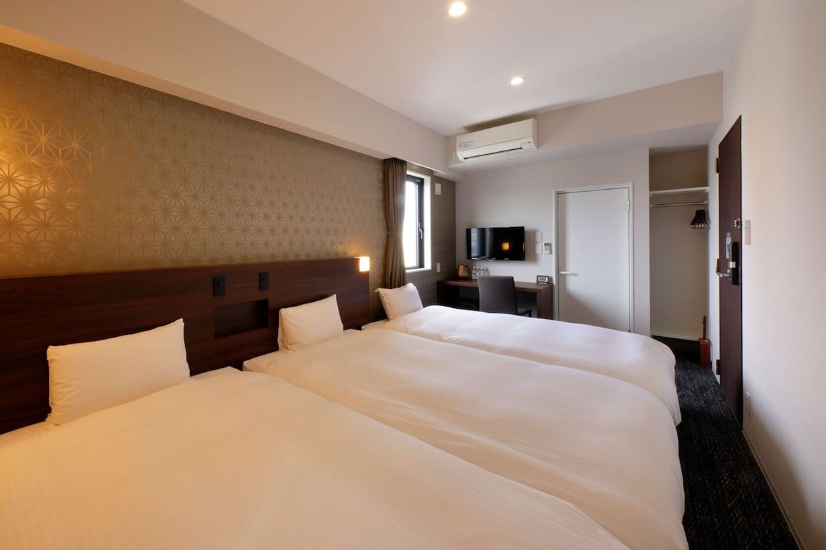 Ein Hotelzimmer mit zwei großen Betten, einem Schreibtisch mit Fernseher und einer Klimaanlage.