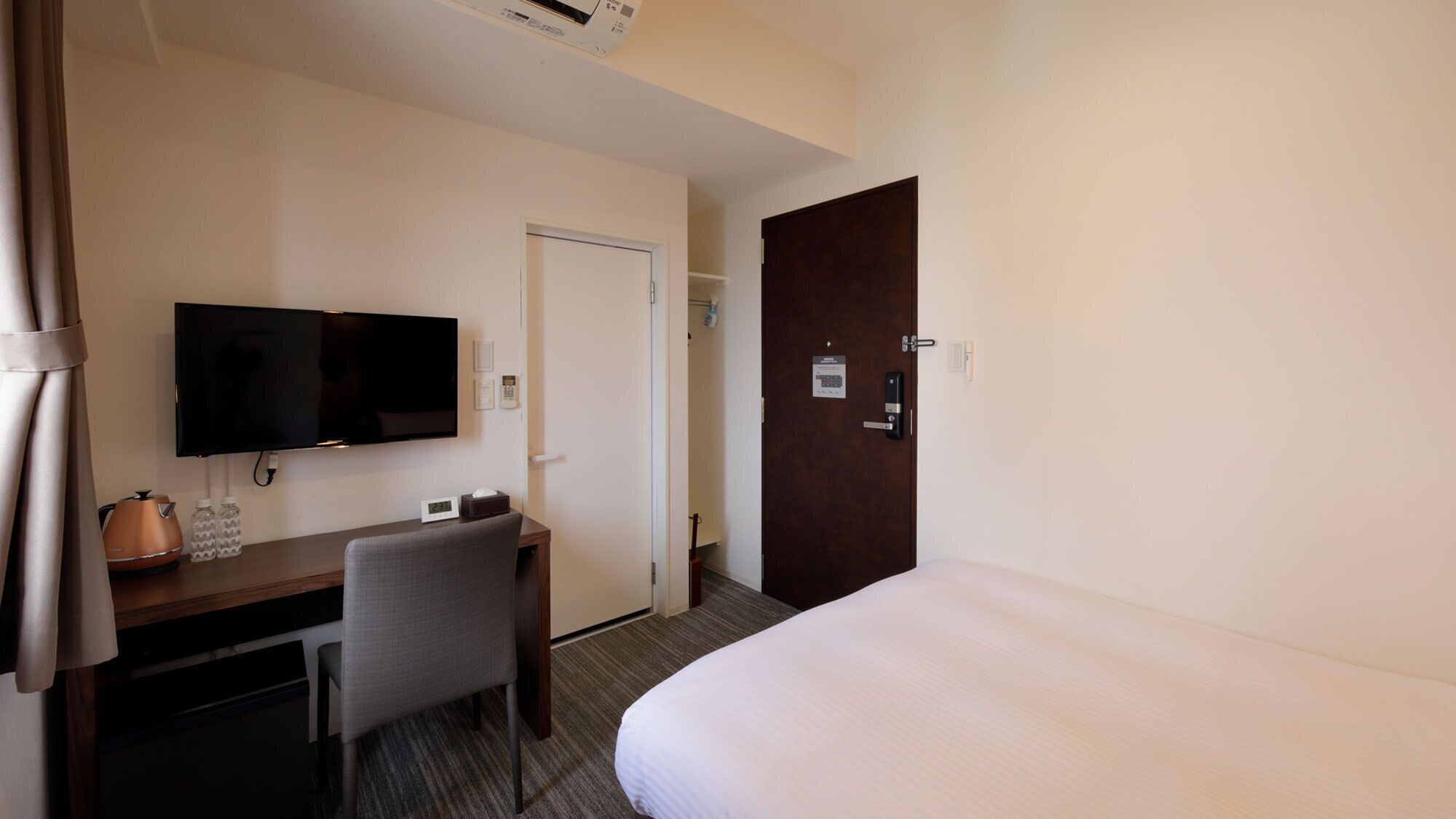 Een hotelkamer met een bed, een bureau met een televisie, een stoel en een deur.
