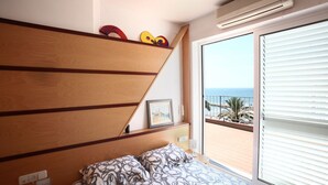 Une chambre à coucher avec un lit, une tête de lit en bois, une fenêtre avec des stores et une vue sur la mer.