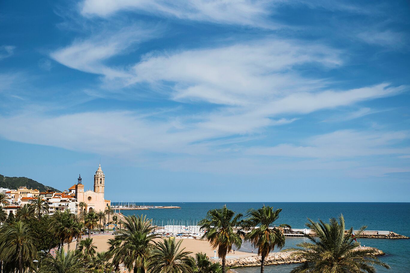 A coastal cityscape with a prominent church tower, a beach with palm trees, and a clear blue sky.