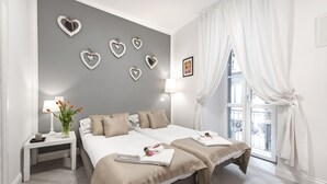 Une chambre d’hôtel avec deux lits, une table de chevet avec une lampe, des décorations murales en forme de cœur et une fenêtre avec des rideaux.