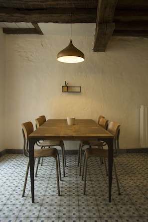 A dining area with a wooden table, six chairs, a hanging pendant light, and a tiled floor.