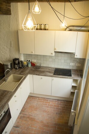 A compact kitchen with white cabinets, a sink, a stove, and hanging pendant lights.