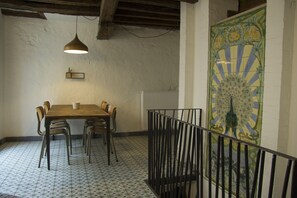 A dining area with a wooden table and chairs, a hanging pendant light, a tiled floor, and a decorative tile mural on the wall.