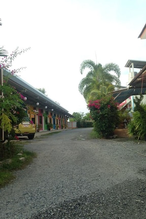 A gravel road leading to a row of colorful buildings with a yellow car parked on the left.