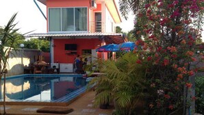 Piscina com deck revestido, rodeada por plantas em vasos e uma palmeira.