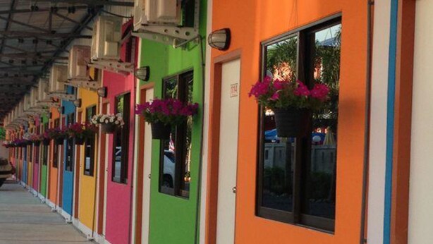 Fileira de quartos de hotel coloridos, cada um com janela e caixas de flores.