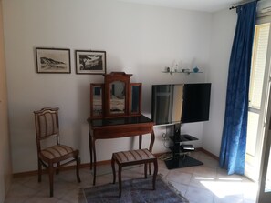 Una habitación con un escritorio de madera, dos sillas, un espejo, un televisor de pantalla plana y dos cuadros en la pared.