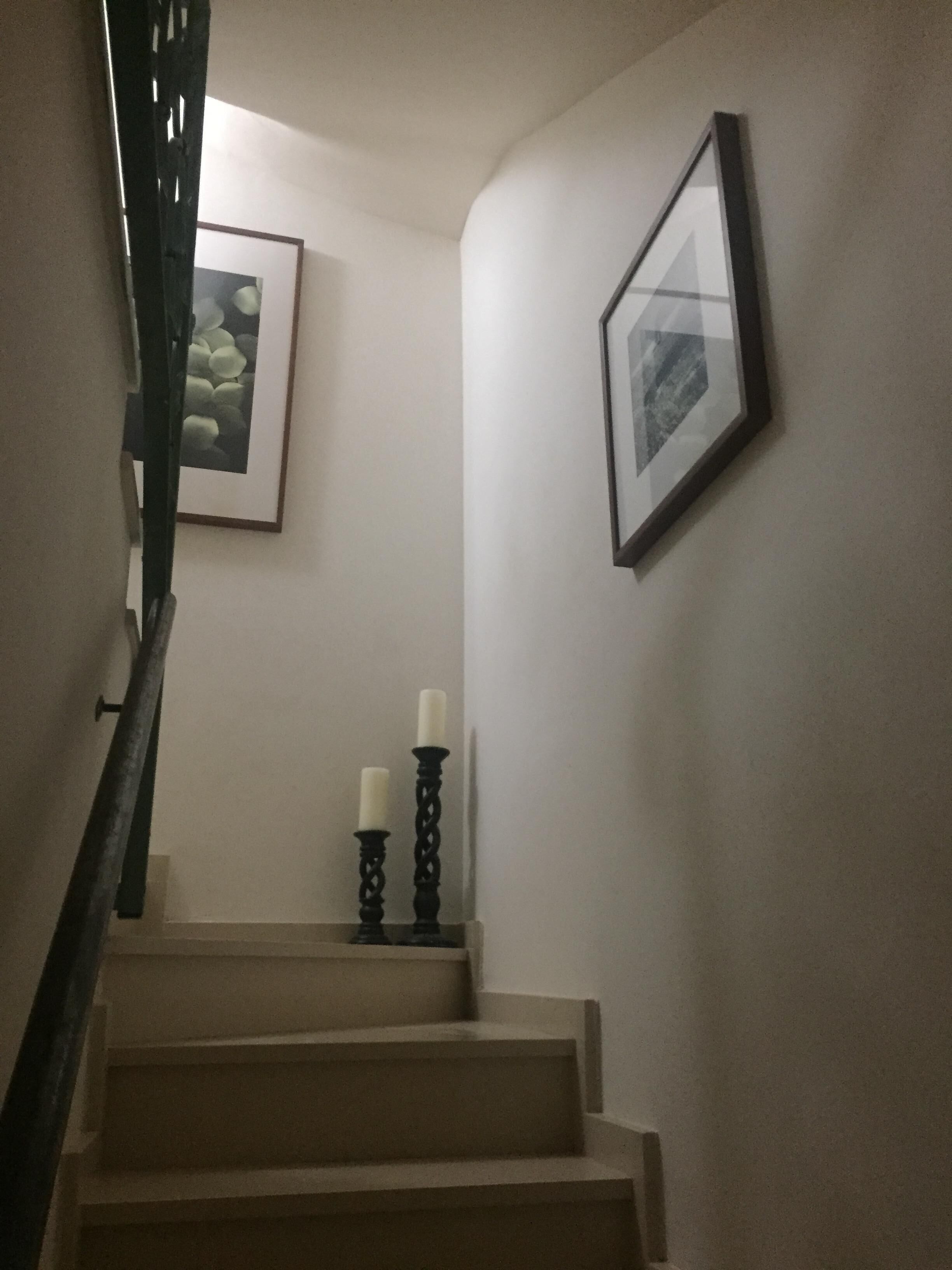 A staircase with a handrail, two lit candles on a stand, and framed pictures on the walls.