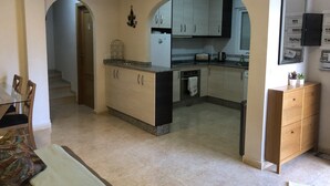 A modern kitchen with a central island, wooden cabinets, and a built-in oven. There is a dining area with a glass table and chairs, and a living room with a sofa and a coffee table. - Stylish Villa, community pool typical Spanish village in La Tercia, Murcia  (Murcia)