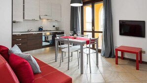 A modern kitchen with white cabinets, a dining area with a red table, and a red sofa.
