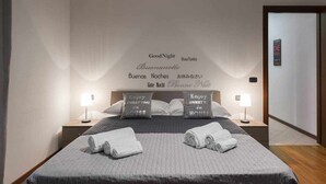 A neatly made bed with pillows, a bedside table with a lamp, and a wall with multilingual 'Good Night' signs.