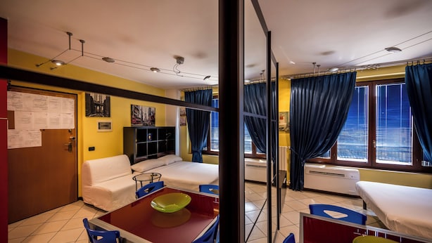 A hotel room with a bed, a desk with a chair, a small table with a bowl, and a window with curtains. - Cozy Suite Arena Milano Santa Giulia (MILANO)