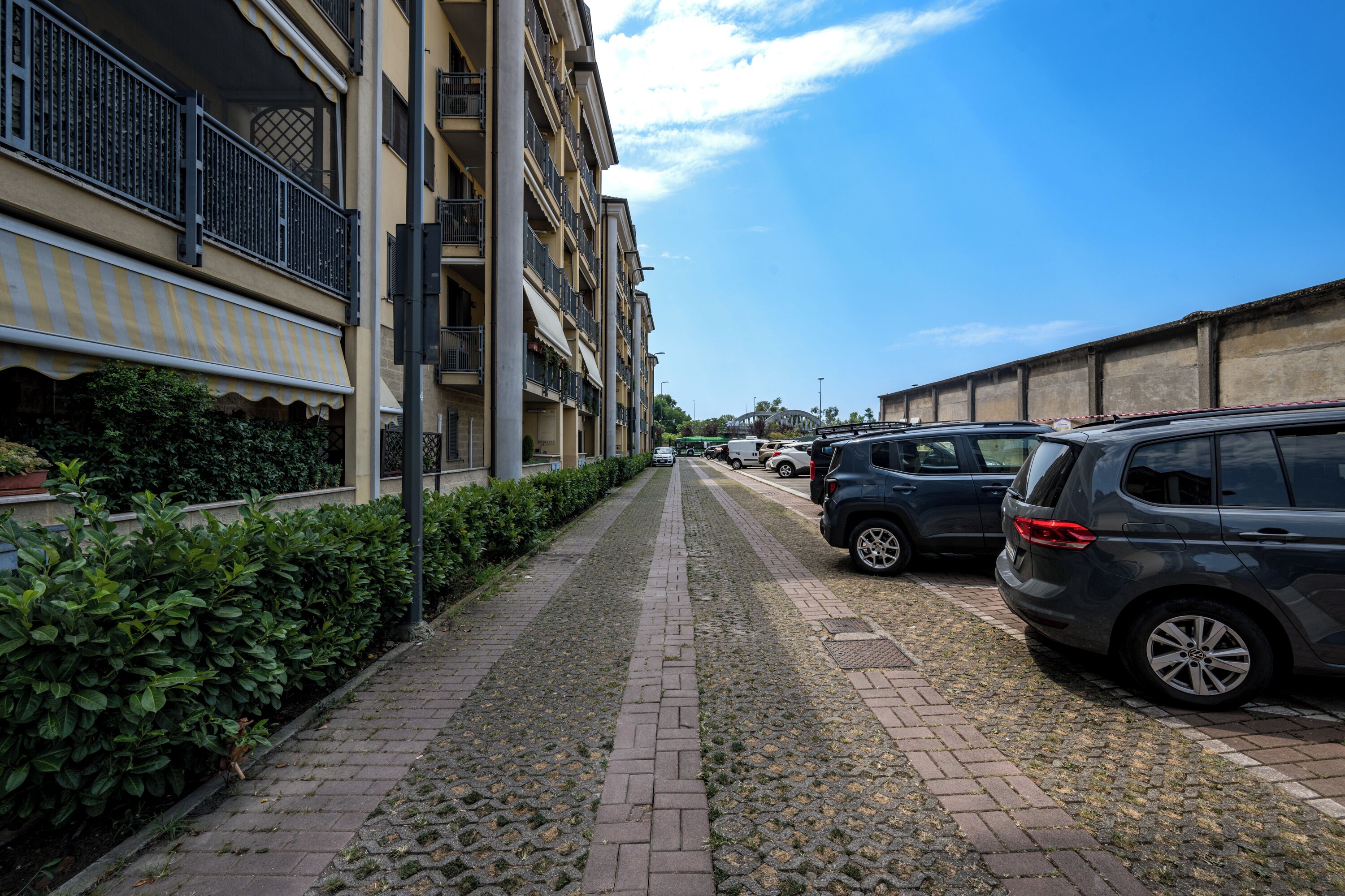 Een verhard pad met geparkeerde auto's aan één kant en een gebouw met balkons aan de andere kant.