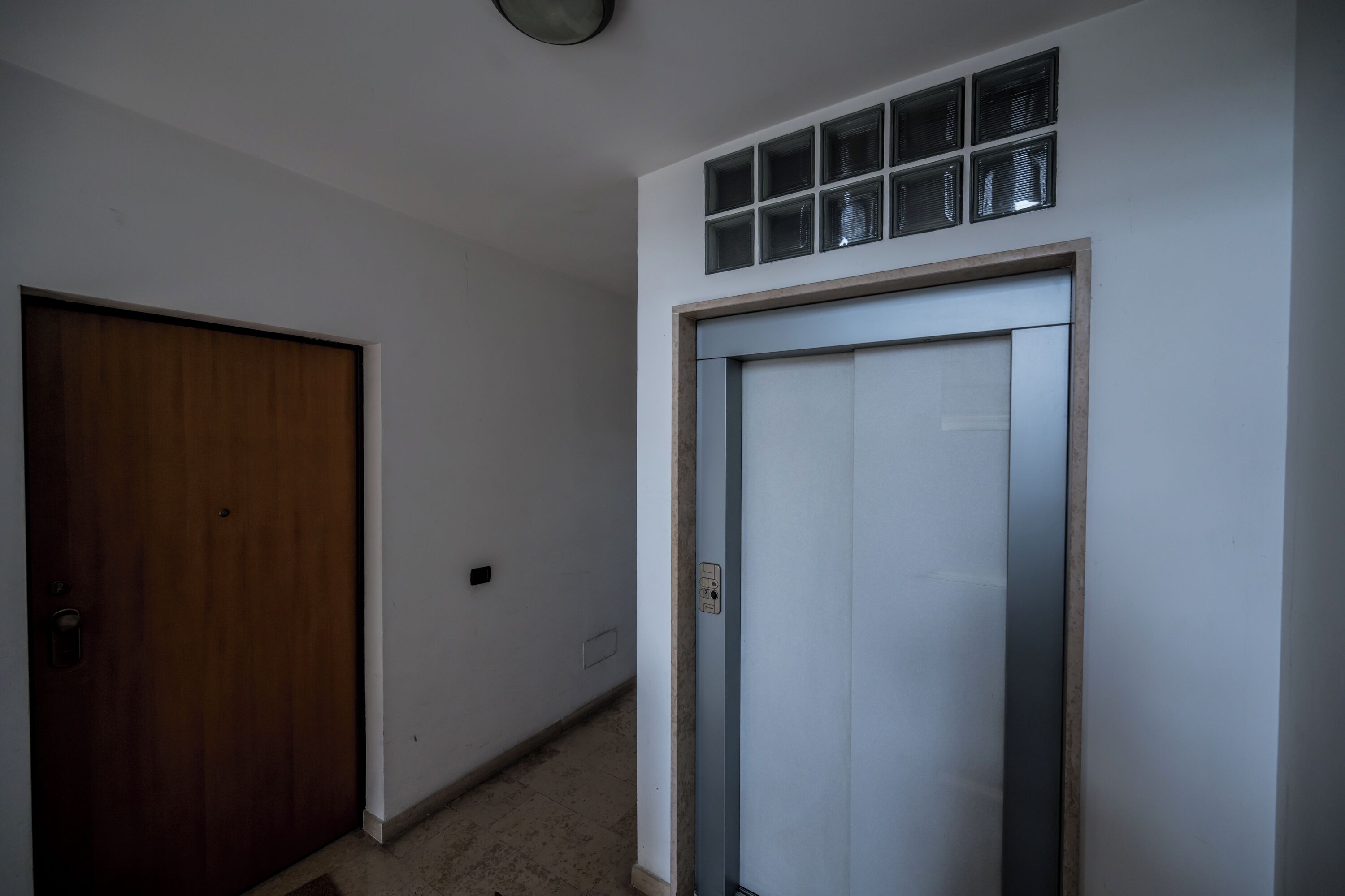 Un couloir avec une porte en bois et un ascenseur blanc.