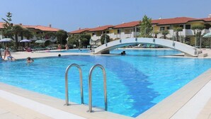 Una piscina con un puente, sillas de descanso y un cielo azul despejado.