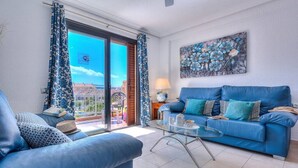 Una sala de estar con un sofá azul, una mesa de centro de cristal y un cuadro en la pared.