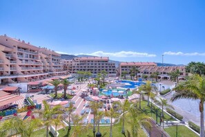 Ein Resort mit mehreren Gebäuden, einem zentralen Poolbereich und Palmen.