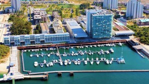 An aerial view of a marina with multiple docks and boats, surrounded by modern buildings and greenery.
