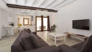 Un salon moderne avec un canapé, une table basse et un téléviseur. Il y a également un coin cuisine avec des tabourets de bar et une table à manger.