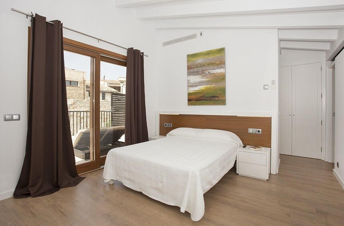 A bedroom with a large bed, a nightstand, a painting on the wall, and a sliding glass door leading to an outdoor area.