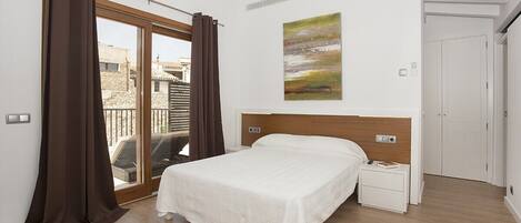 A bedroom with a large bed, a nightstand, a painting on the wall, and a sliding glass door leading to an outdoor area.