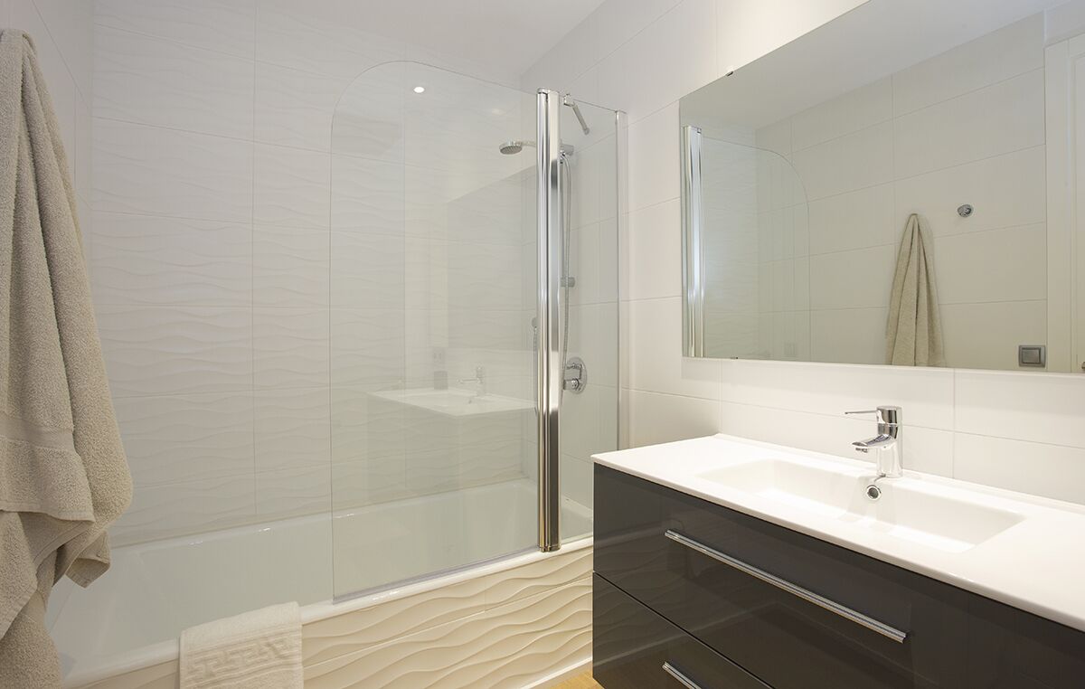 A modern bathroom with a glass-enclosed shower, a white sink, and dark-toned cabinets.