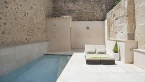 Un espace aménagé au bord de la piscine, avec un mur en pierre, un canapé blanc agrémenté de coussins et une plante en pot.