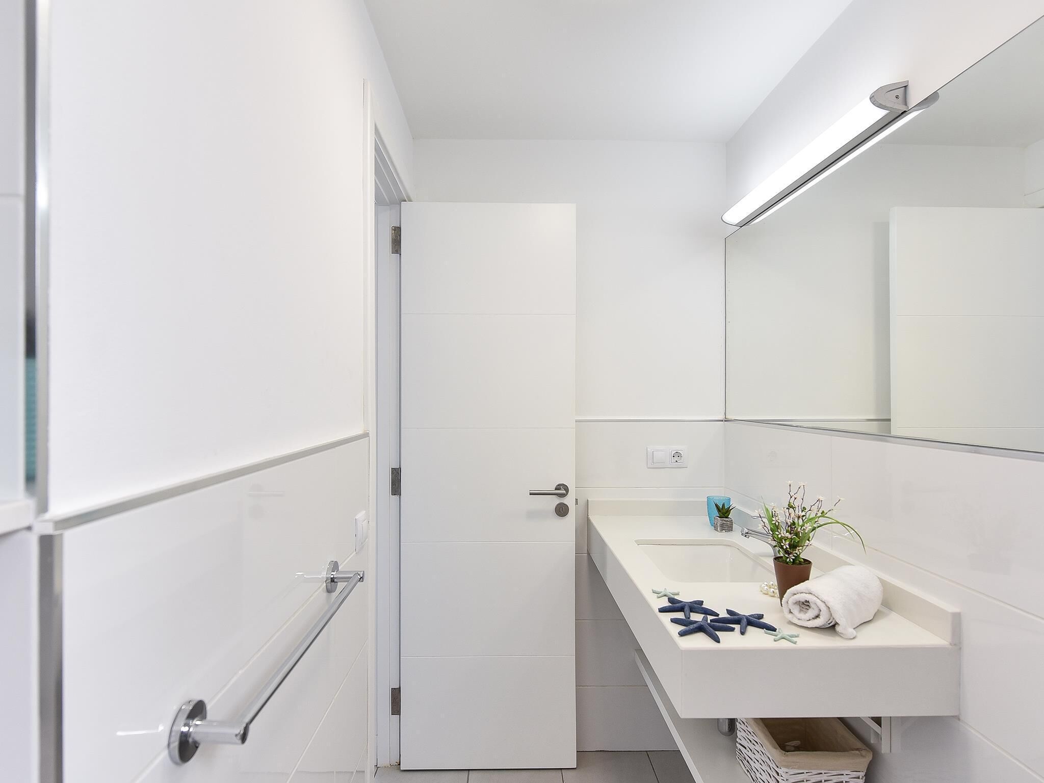 Une salle de bain moderne avec un lavabo blanc, un miroir et un porte-serviettes.