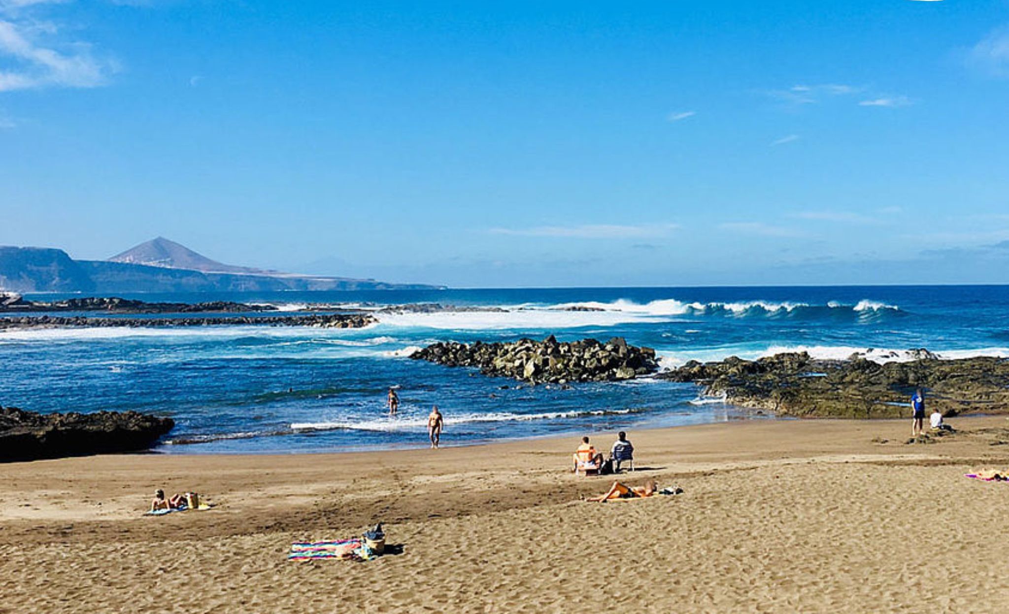 A beach scene with clear skies, waves, and rocky outcrops.