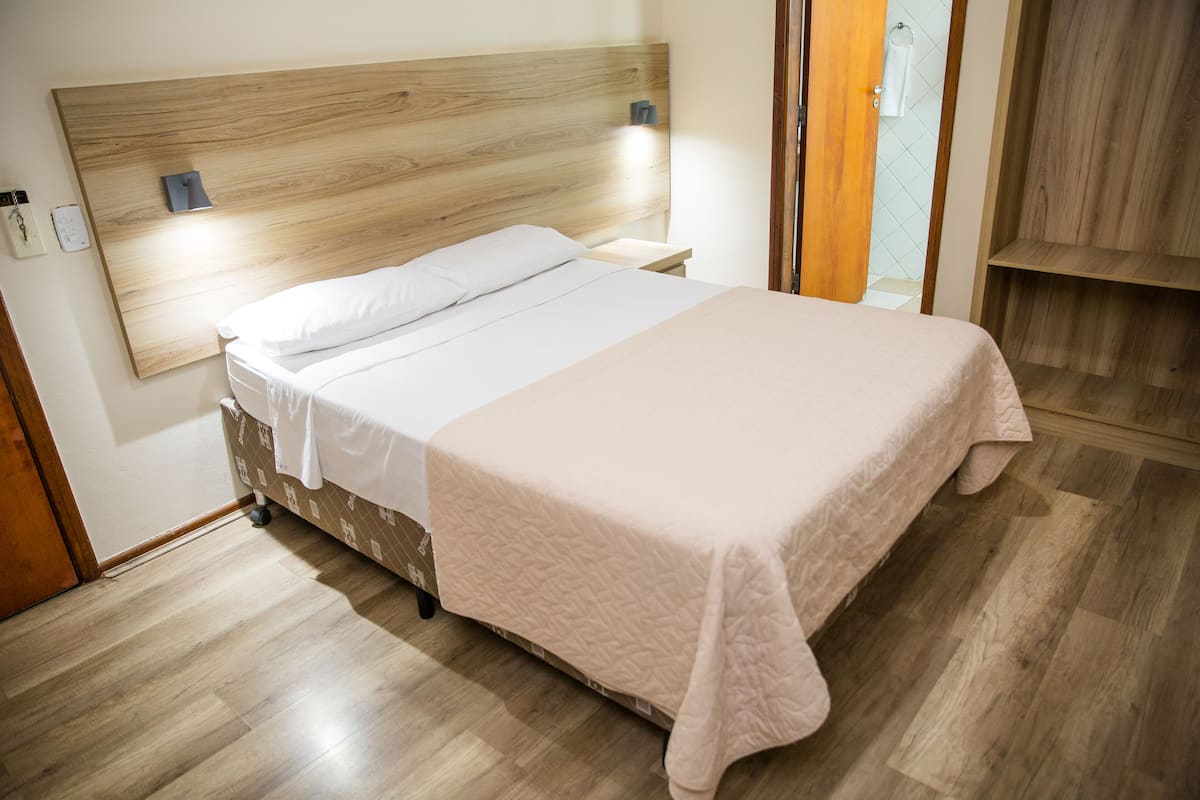 Un lit bien fait, avec une tête de lit en bois, une table de chevet avec une lampe et un plancher en bois.