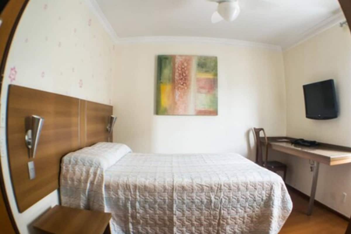Une chambre à coucher comprenant un lit, un bureau, une chaise, un téléviseur et un ventilateur de plafond.